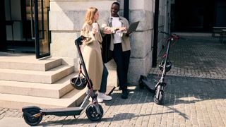 Two people with their F3 Pro scooters parked up while they drink cafe and work on a laptop