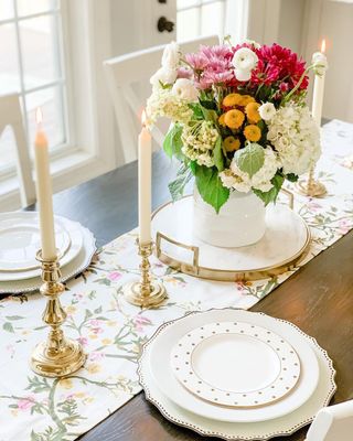 Candle sticks in gold holders with floral table runner and beautiful display of seasonal flowers