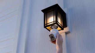 A Wyze Bulb Cam being held by a hand screwed into a black iron outdoor light fixture