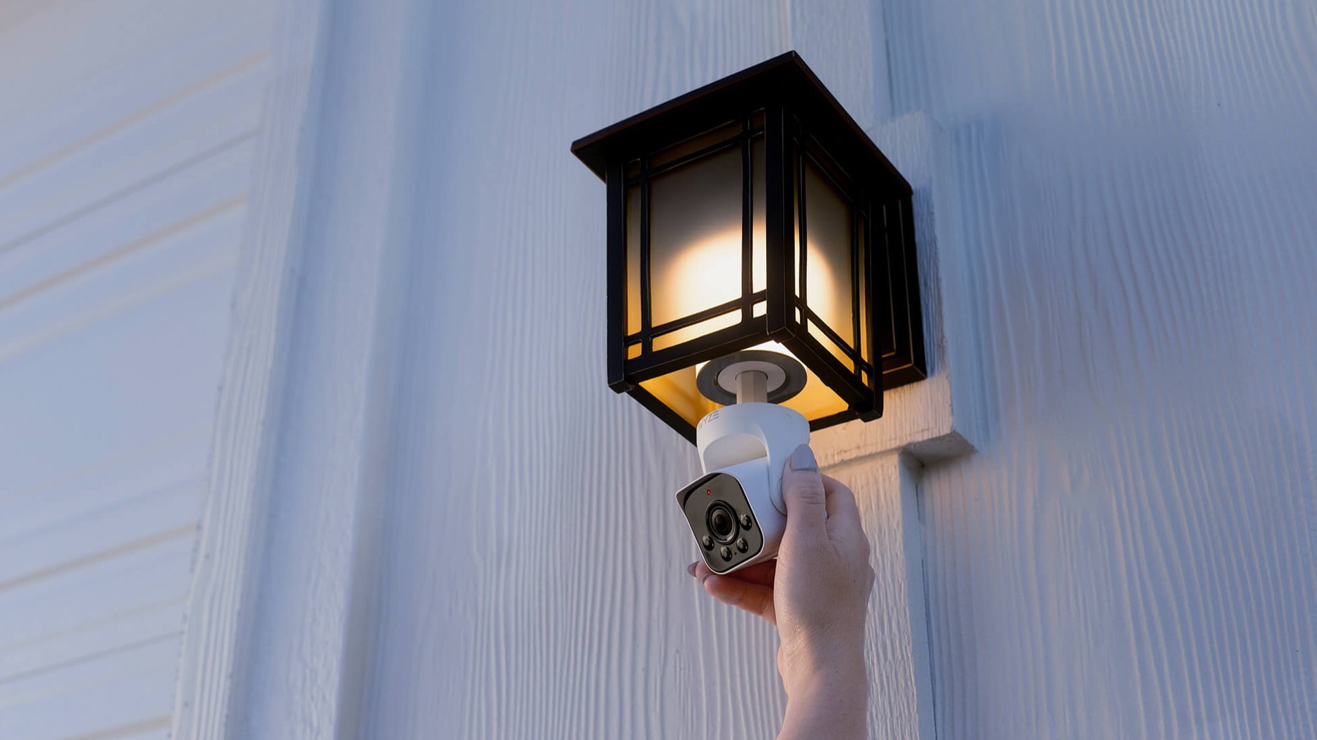 A Wyze Bulb Cam being held by a hand screwed into a black iron outdoor light fixture