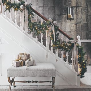 A staircase in the hallway decorated with large grey ribbon tied into bows and light-up Christmas garland