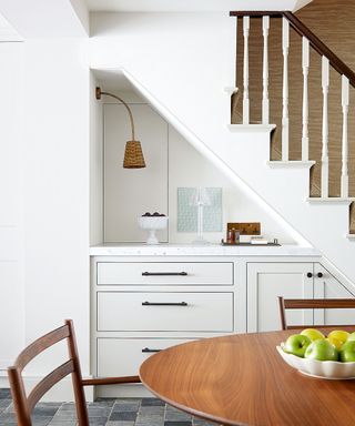 Under stairs storage, cabinets and countertop, round wooden dining table, white staircase