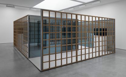 Installation view of Greek Meander Pavilion, room with slate grey floor, white walls, suspended white ceiling with skylights and spotlights around the edge, wooden frame construction with blue glass panel dividers and white floor