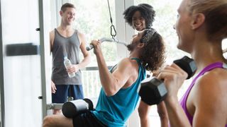 Man performing lat pull-down in gym surrounded by other gym-goers
