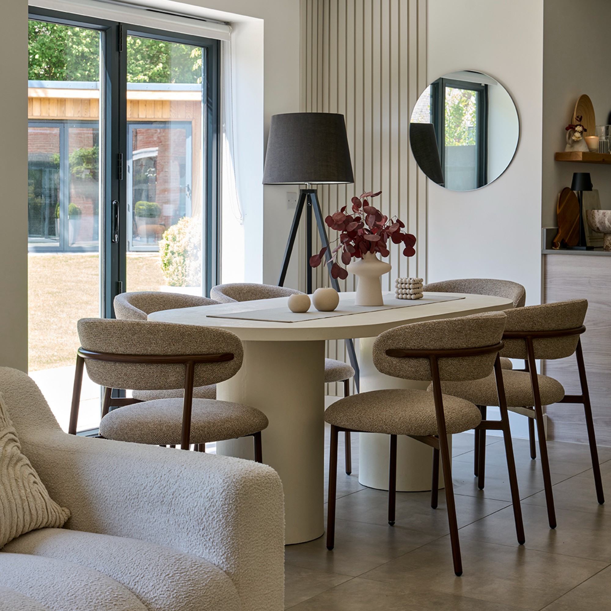 A dining area within an open-plan home with an oval dining table with pillar legs and upholstered dining chairs