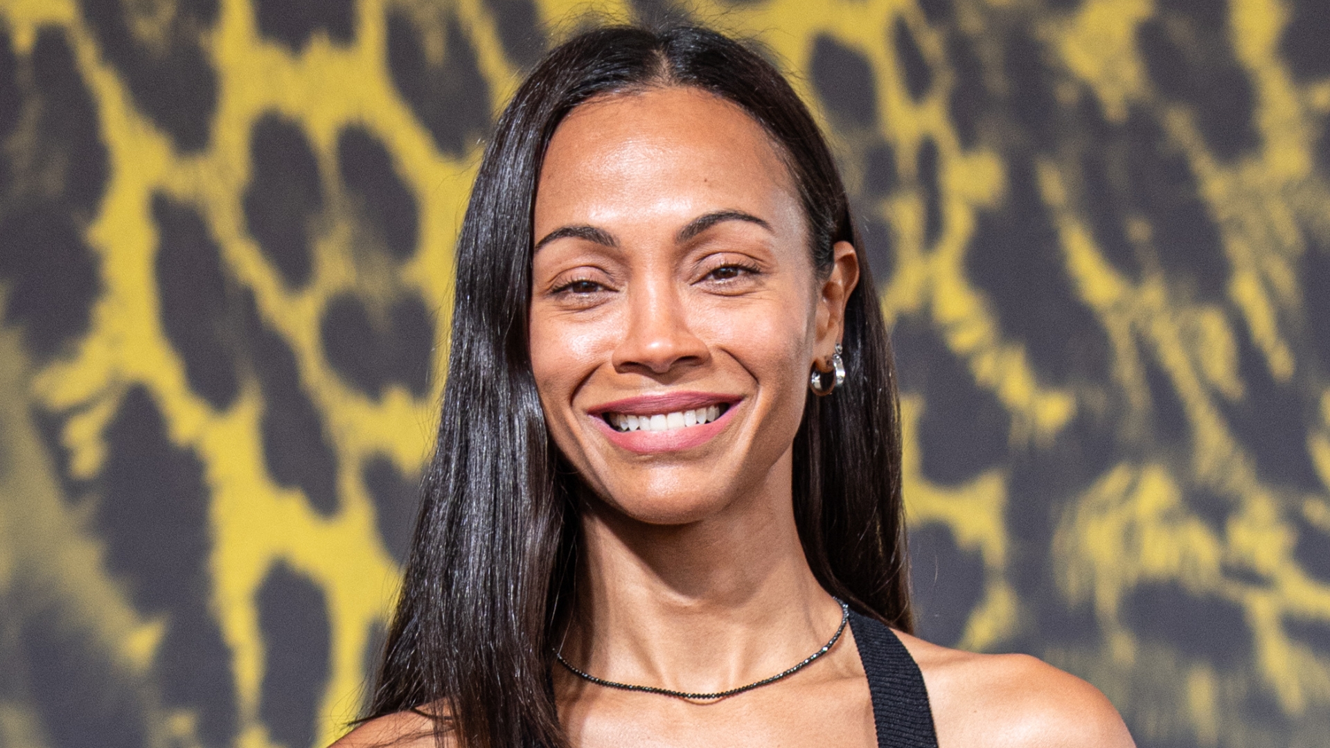 Image of Zoe Saldana smiling with long straight black hair tucked behind one shoulder