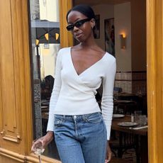 Influencer @sylviemus_ wears a white wrap cardigan with cigarette jeans and black mules.