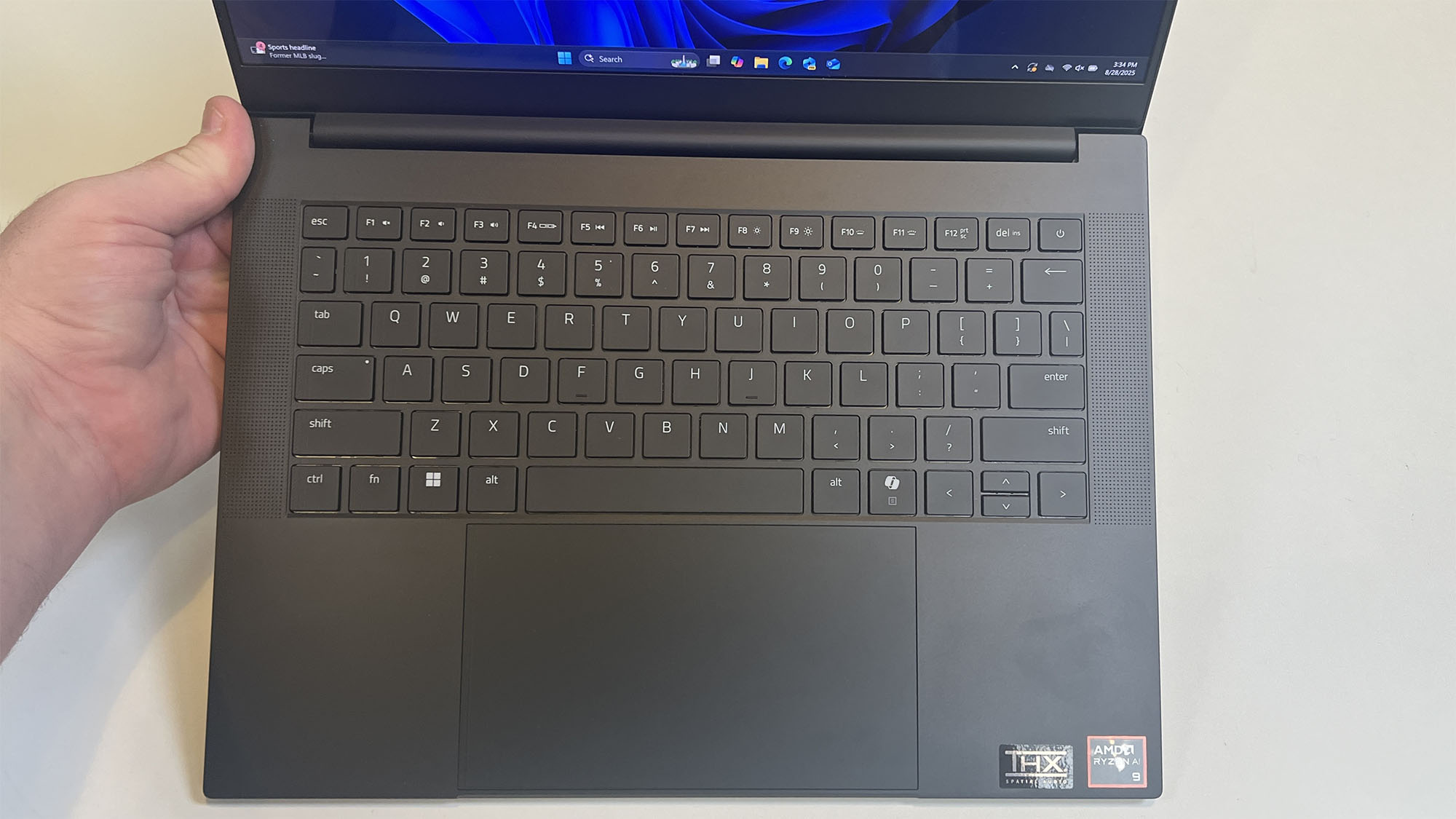 A masculine hand tilting the Razer Blade 14 (2025) upward to show off the keyboard