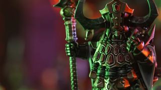 A Helsmith of Hashut model bathed in green light and holding a staff holds up a clenched fist