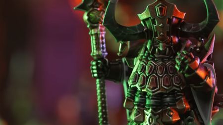 A Helsmith of Hashut model bathed in green light and holding a staff holds up a clenched fist