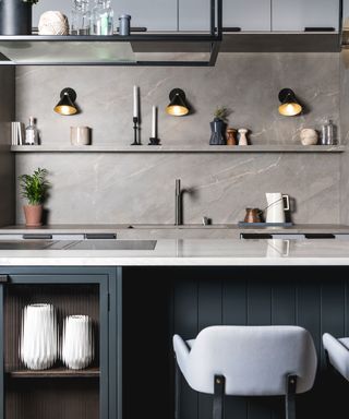 An example of modern kitchen lighting ideas showing a close up shot of a dark kitchen island with white worktops and white bar stools
