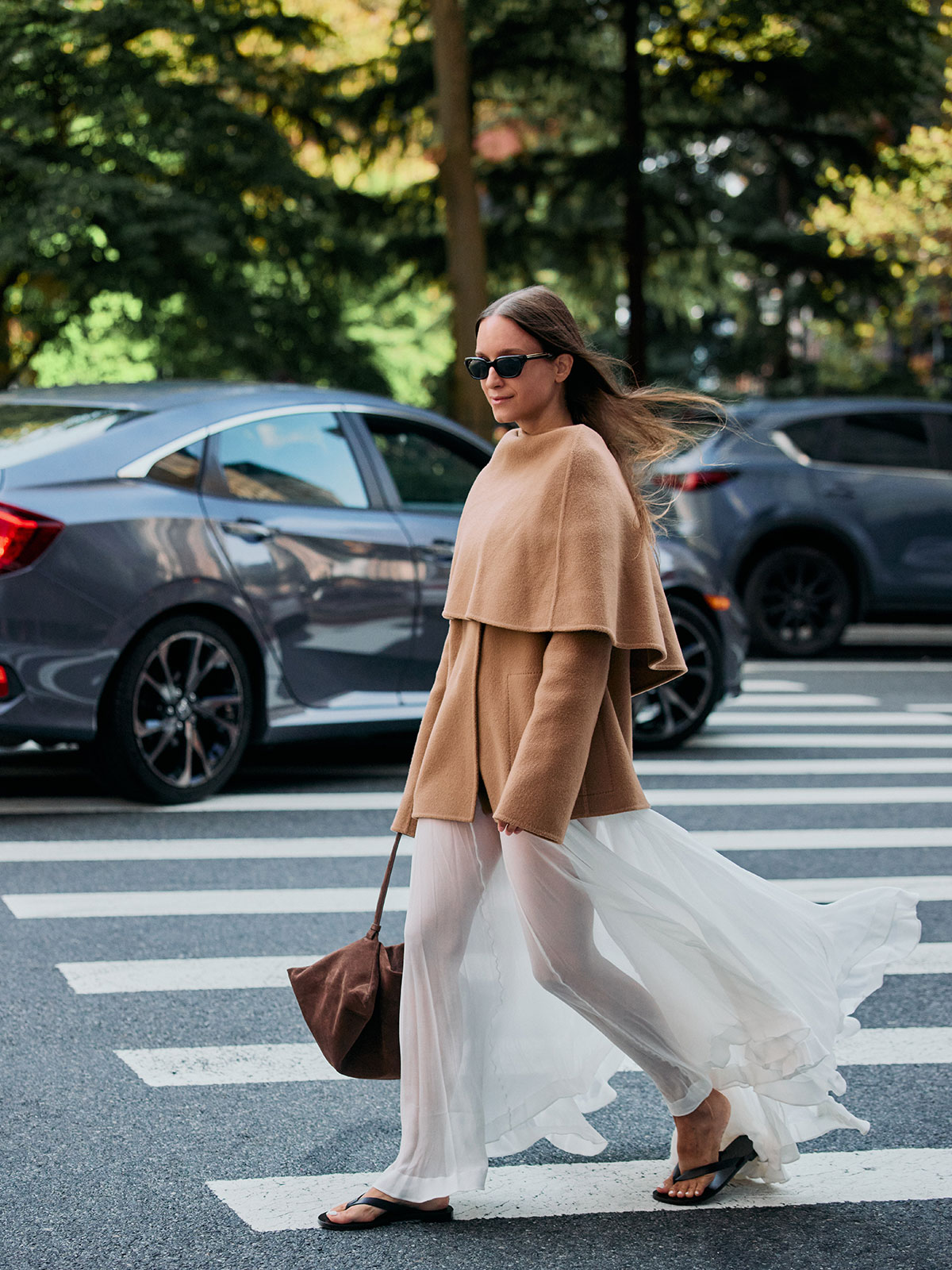 Woman wearing a tan cape coat and white sheer skirt.