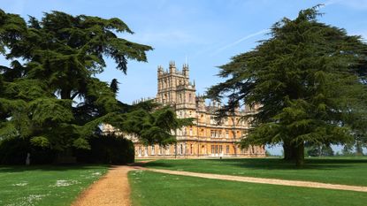 The exterior of Highclere Castle on a sunny day framed with two massive trees