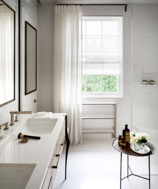A white bathroom with a curtain beside the window and a double vanity unit