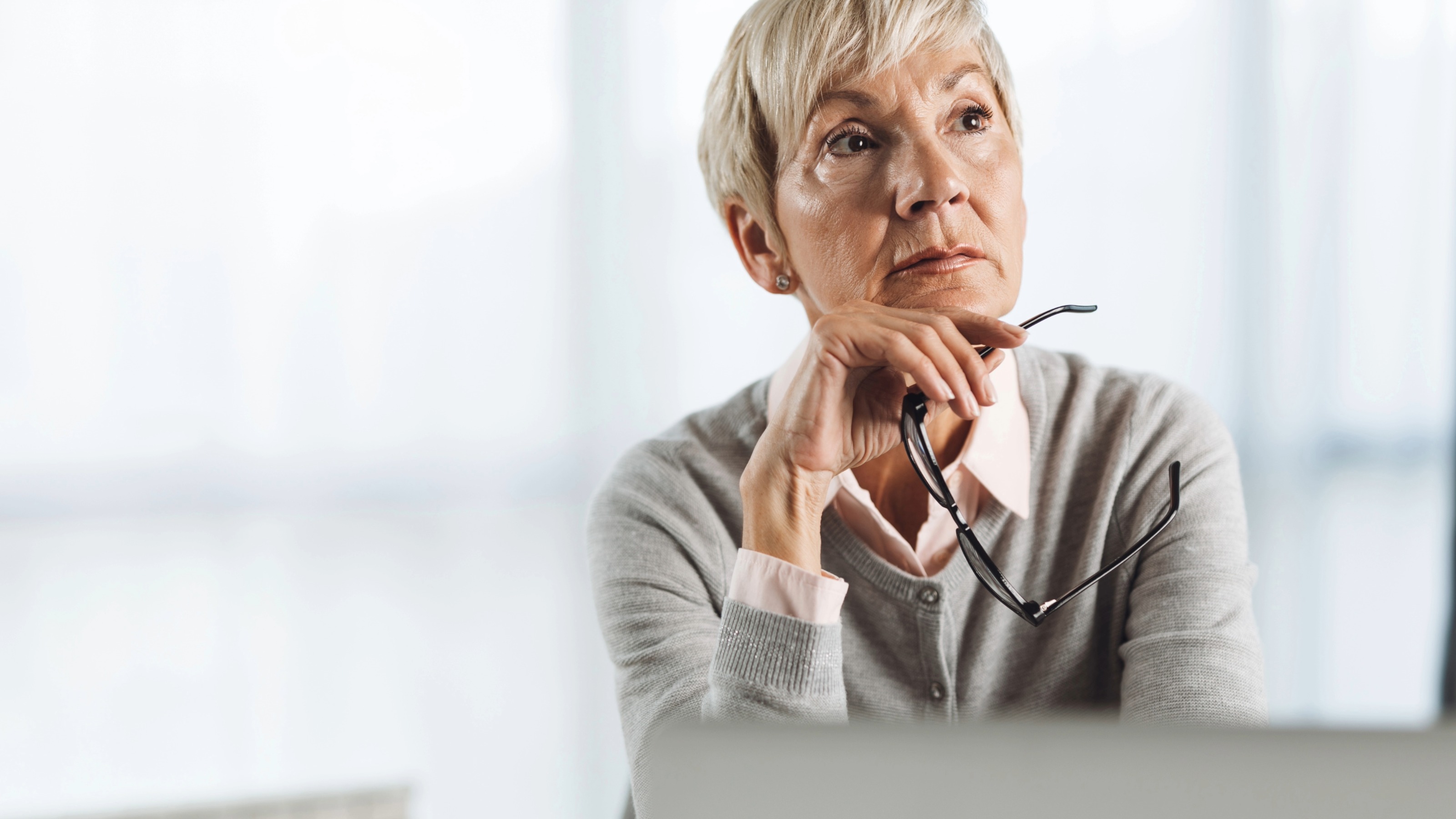 Pensive senior woman thinking while working on laptop in the office