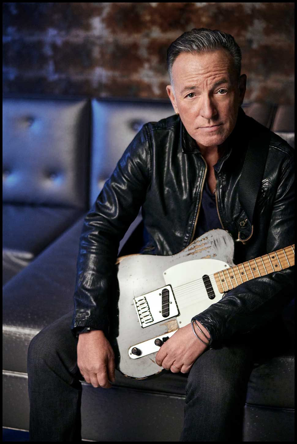 Bruce Springsteen posing on a sofa with a guitar