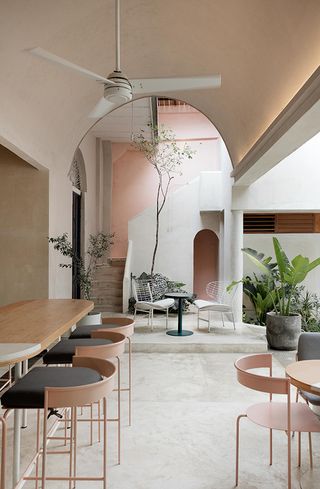 Extraño cafe with high arched ceiling and fan, pot plants and stairway with blush wall