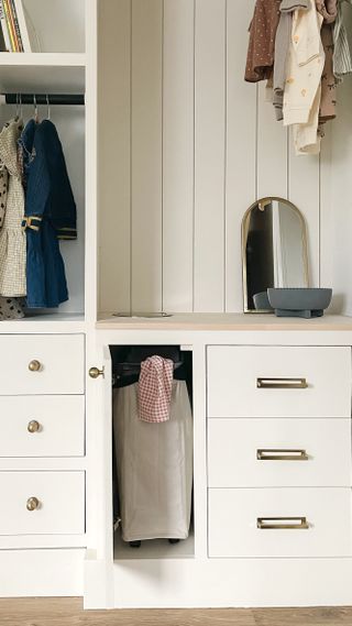 A kid's closet with an open cabinet revealing a concealed laundry basket