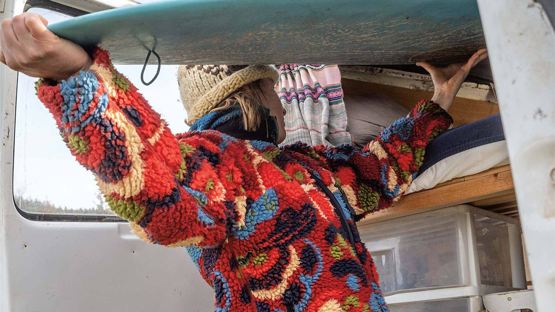 Woman putting away a surfboard wearing a Patagonia fleece jacket