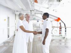 A senior couple shake hands with the captain on a cruise ship.