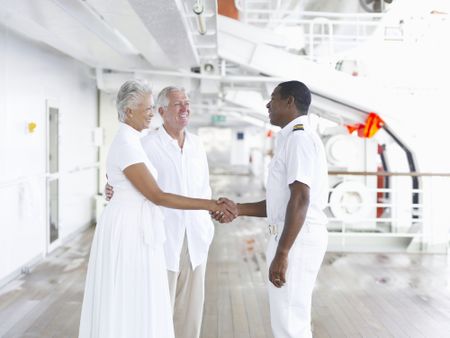 A senior couple shake hands with the captain on a cruise ship.
