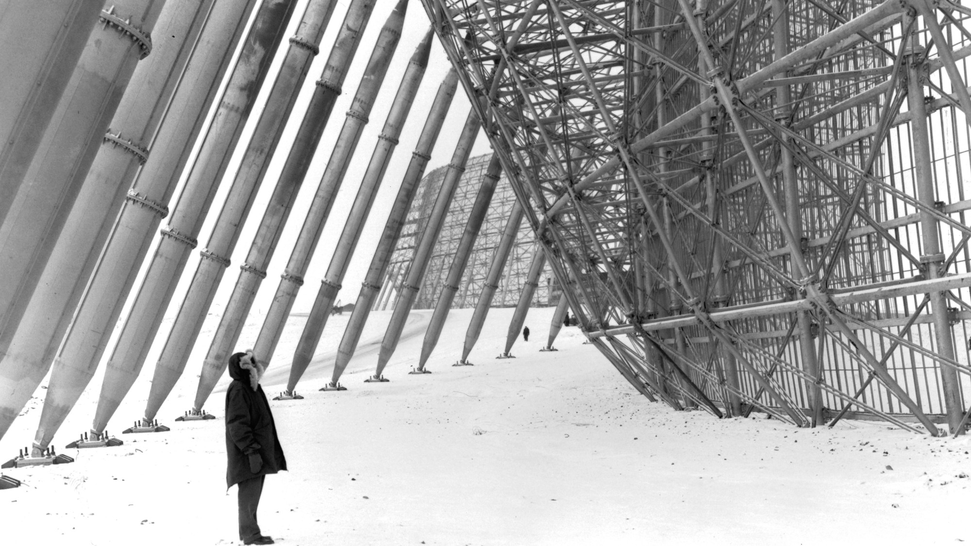 figure standing next to large metal supports and bottom of a radar antennae
