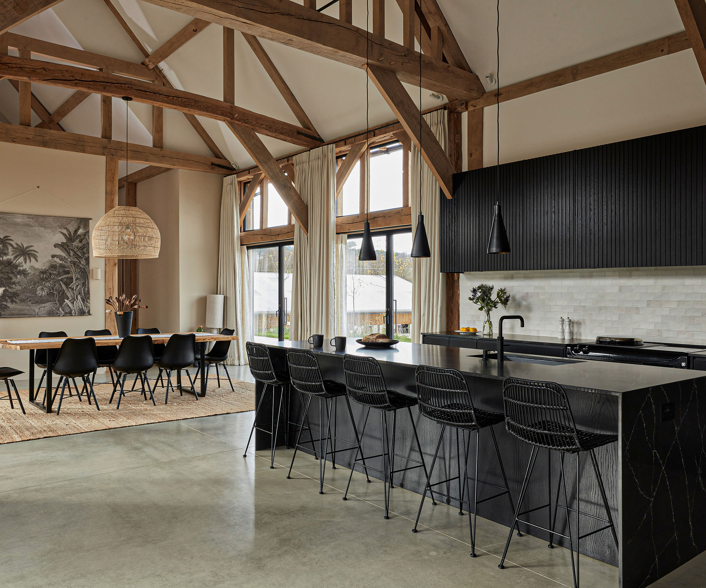 black fluted open plan kitchen diner with vaulted ceiling and exposed timber beams with polished concrete floor