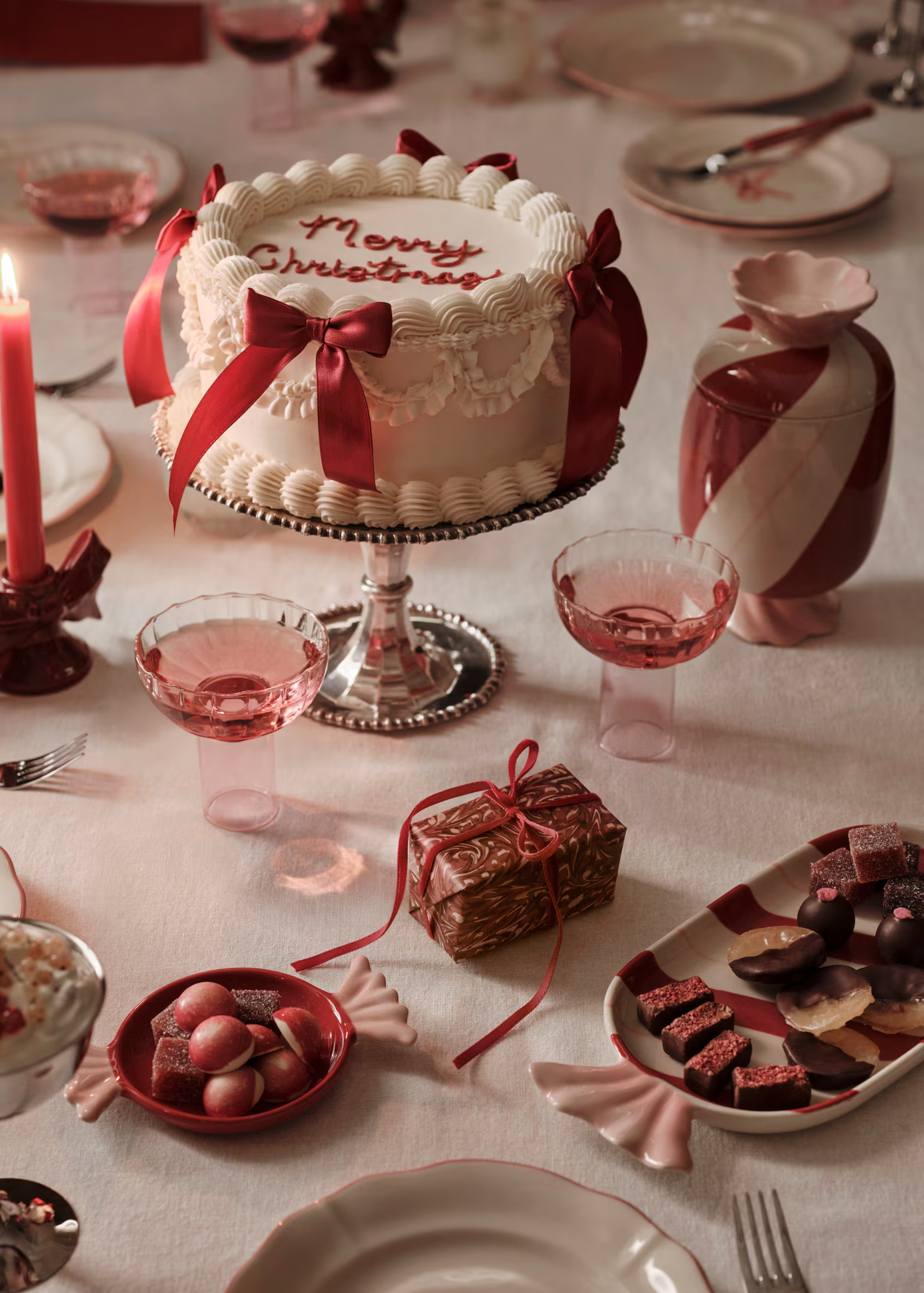 A table set with a white tablecloth with a cake with bows, candy themed plates, coupes, and snacks