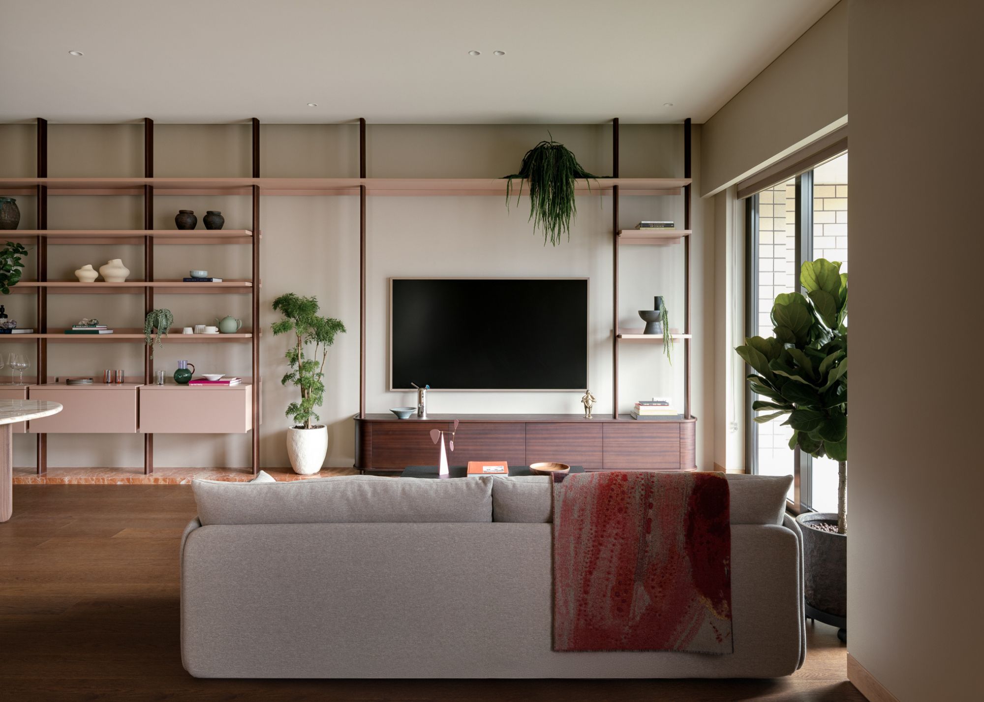 A bright, airy living room in a Hong Kong apartment with potted plants, open shelves, and a couch