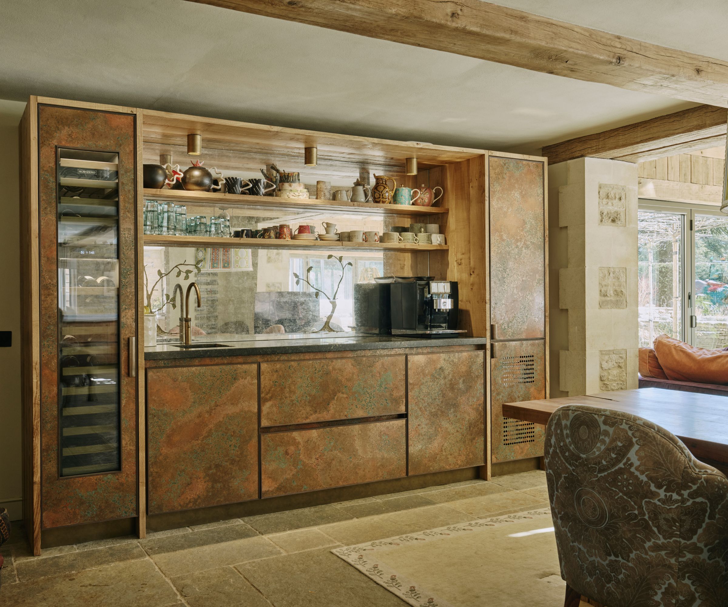 The dining area of an open plan kitchen in the Cotswolds featuring a metallic breakfast bar area with blue marble countertops and a mirrored backsplash