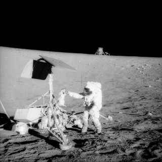 Astronaut Pete Conrad examines the camera on Surveyor 3, with the Apollo 12 spacecraft in the background.