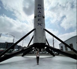 a woman stands beneath a massive rocket with the word "SpaceX" on it
