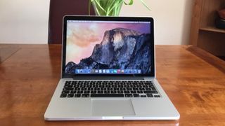 En MacBook Pro (13 tum, 2020) står öppnad på ett träfärgat bord.