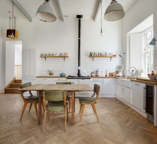 Wooden kitchen floor with kitchen table and green chairs. White units with stove