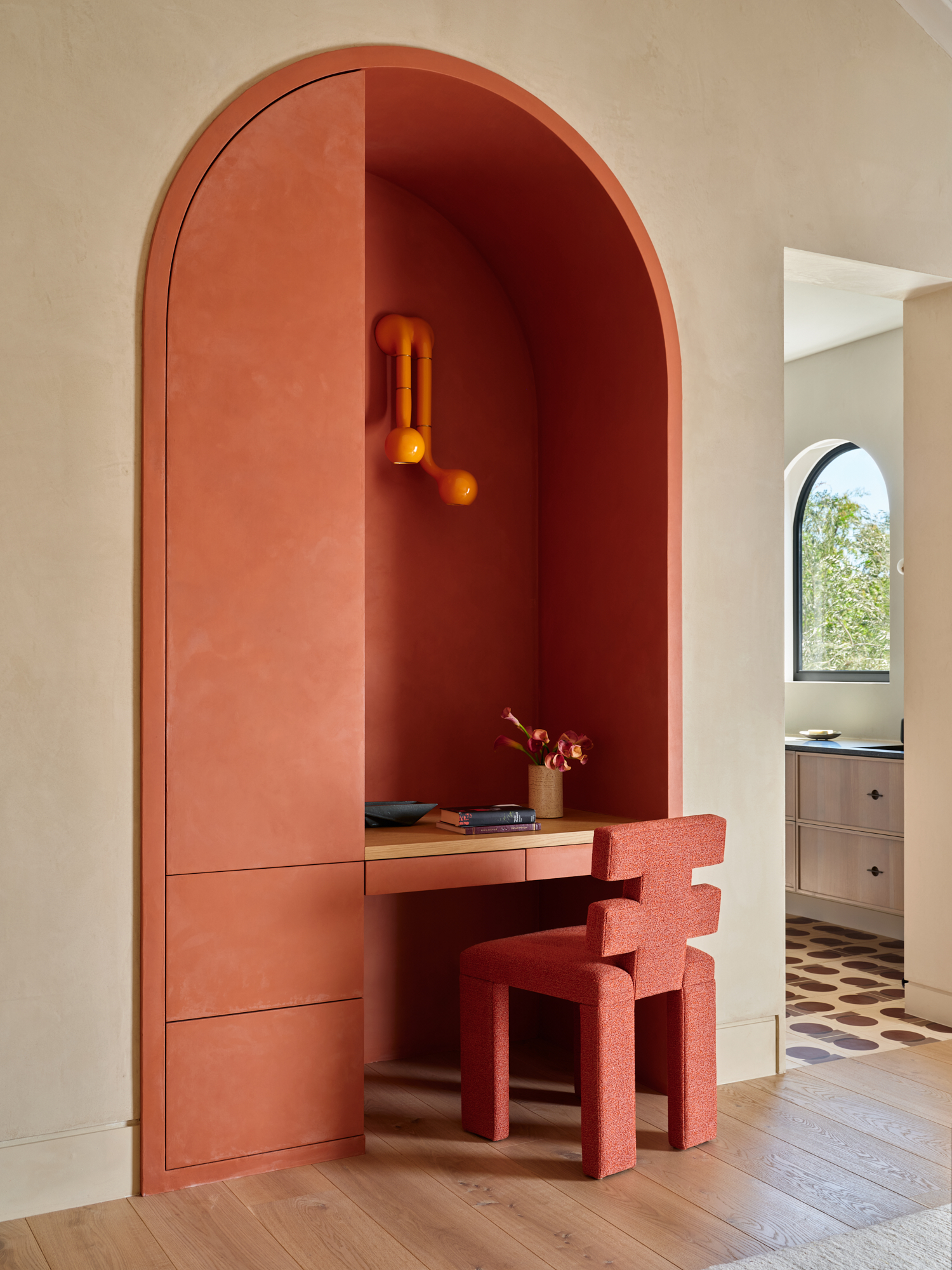 Image of a room with white walls, but there is a built-in desk area that is painted in a bright coral color. There is a matching coral desk chair.