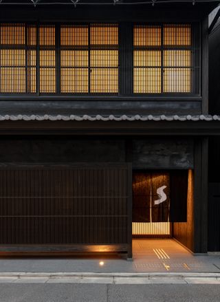 Close up view of the black entrance at the Shinmonzen hotel in Kyoto. The lights are on and there is a white 'S' on a split black curtain hanging at the doorway