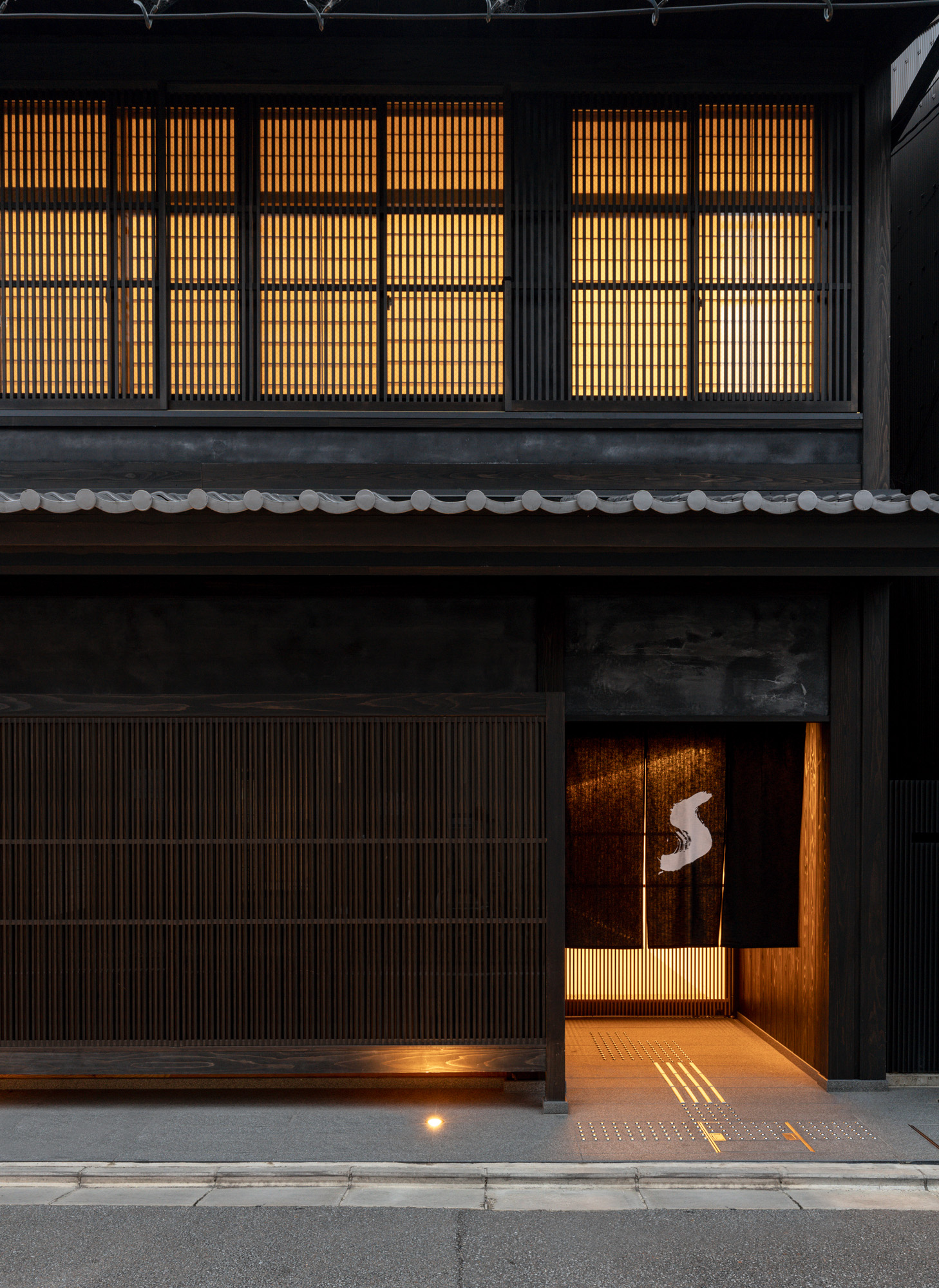 Close up view of the black entrance at the Shinmonzen hotel in Kyoto. The lights are on and there is a white 'S' on a split black curtain hanging at the doorway