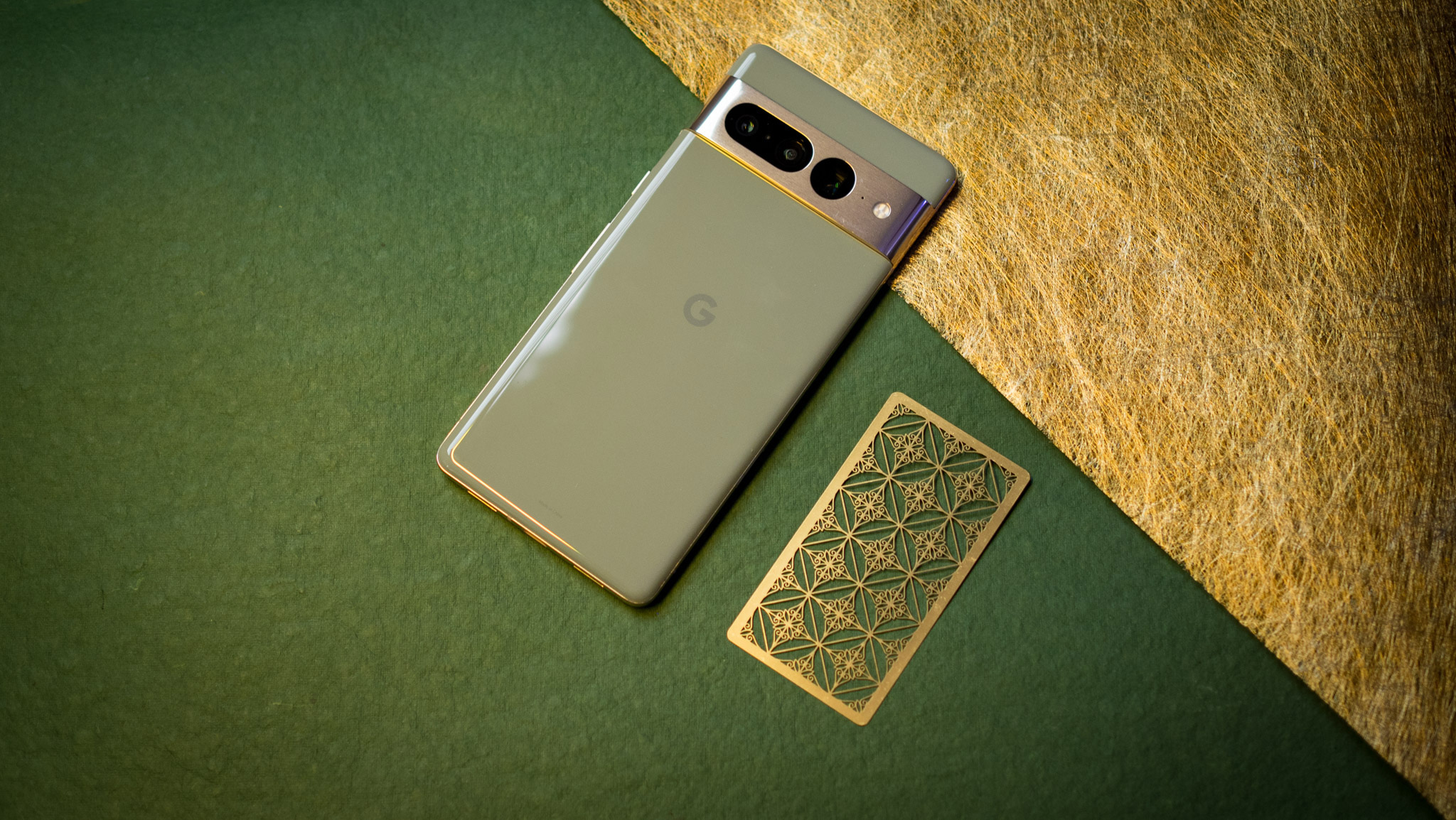 Google Pixel 7 Pro back view on green background next to gold bookmark