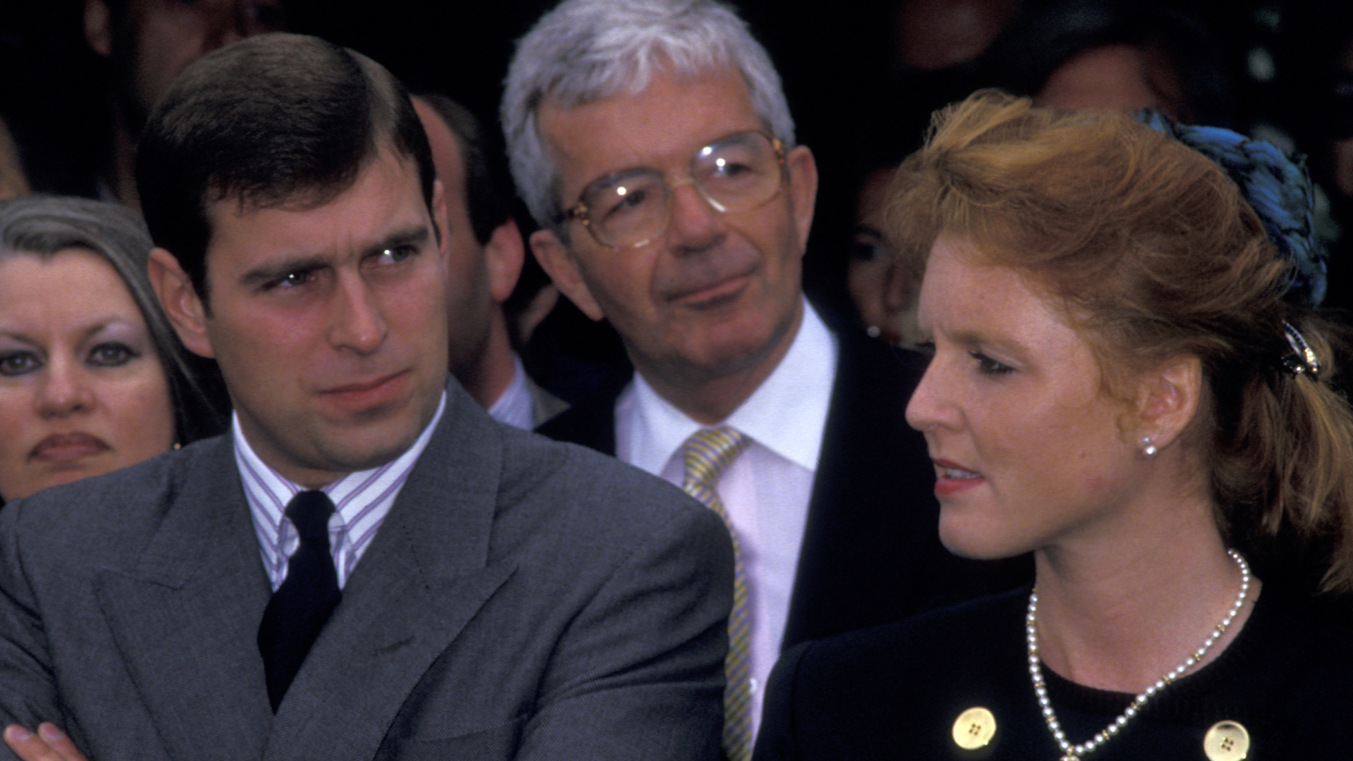 Prince Andrew wearing a gray suit, folding his arms and frowning standing next to Sarah Ferguson