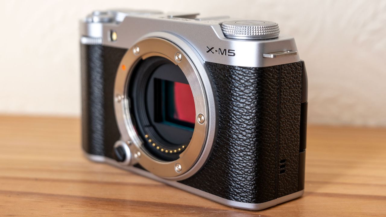The Fujifilm X-M5 at a diagonal angle on a wooden shelf.