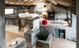 A hotel bedroom with steps to 2 lower platforms, a bed, a bar fridge, a fireplace, a zebra skin rug, stone walls and a wooden ceiling.