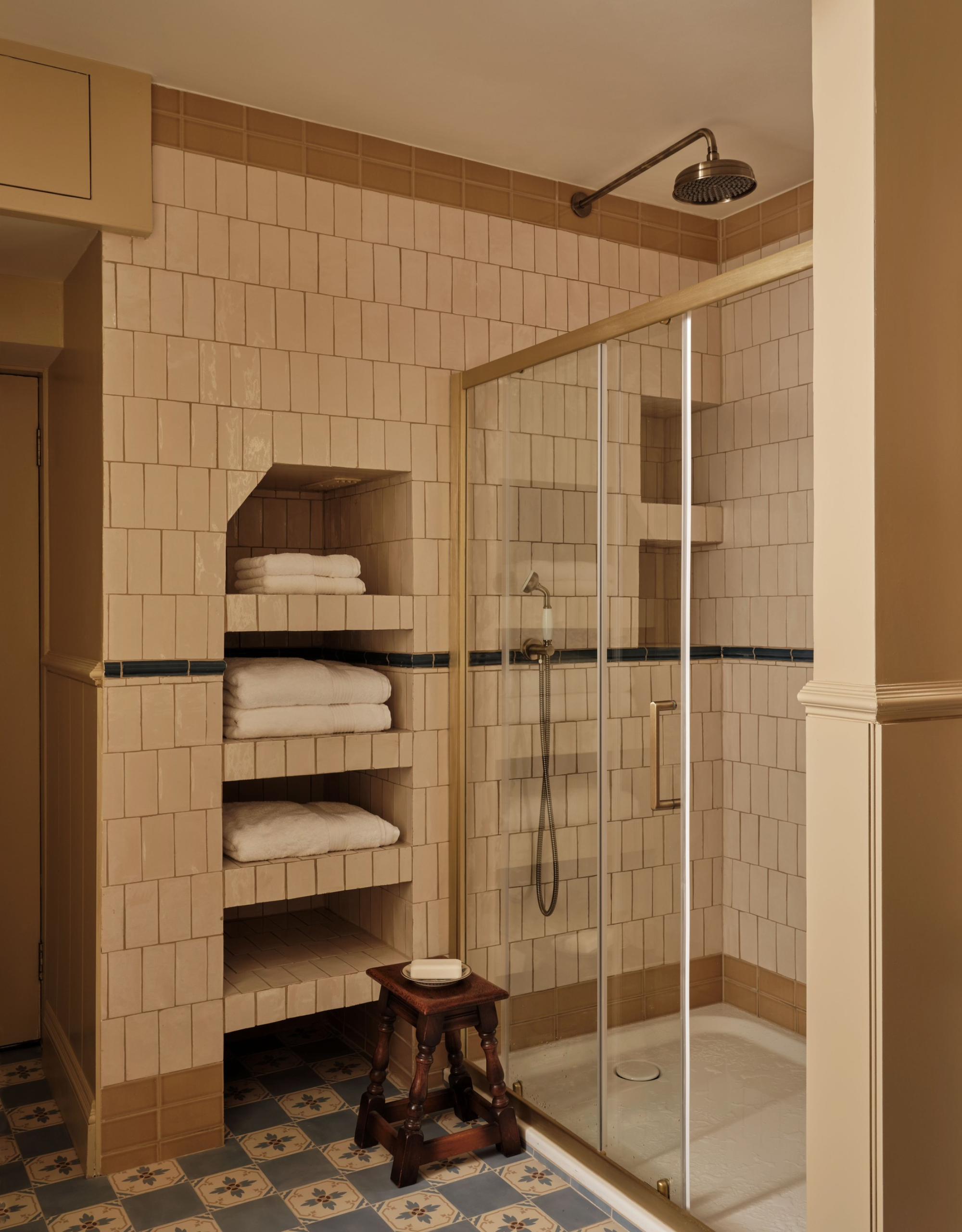 a tiled bathroom with a wooden stool, built-in shelves and an enclosed shower