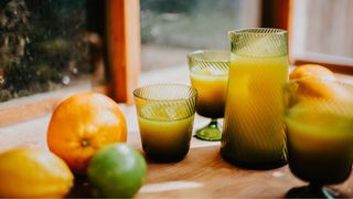 Oranges, whole and in fruit juice, sitting in glasses and carafes on table in the sunshine