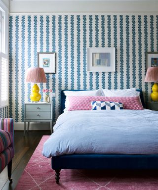 Blue and pink bedroom with blue patterned striped wallpaper, pink and yellow accessories