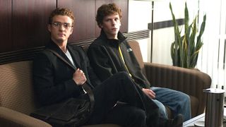 A still from the movie The Social Network showing Justin Timberlake and Jesse Eisenberg sitting side-by-side on a brown sofa.