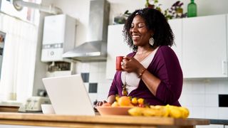 Woman smiling and drinking from a cup on a video call at home with friends