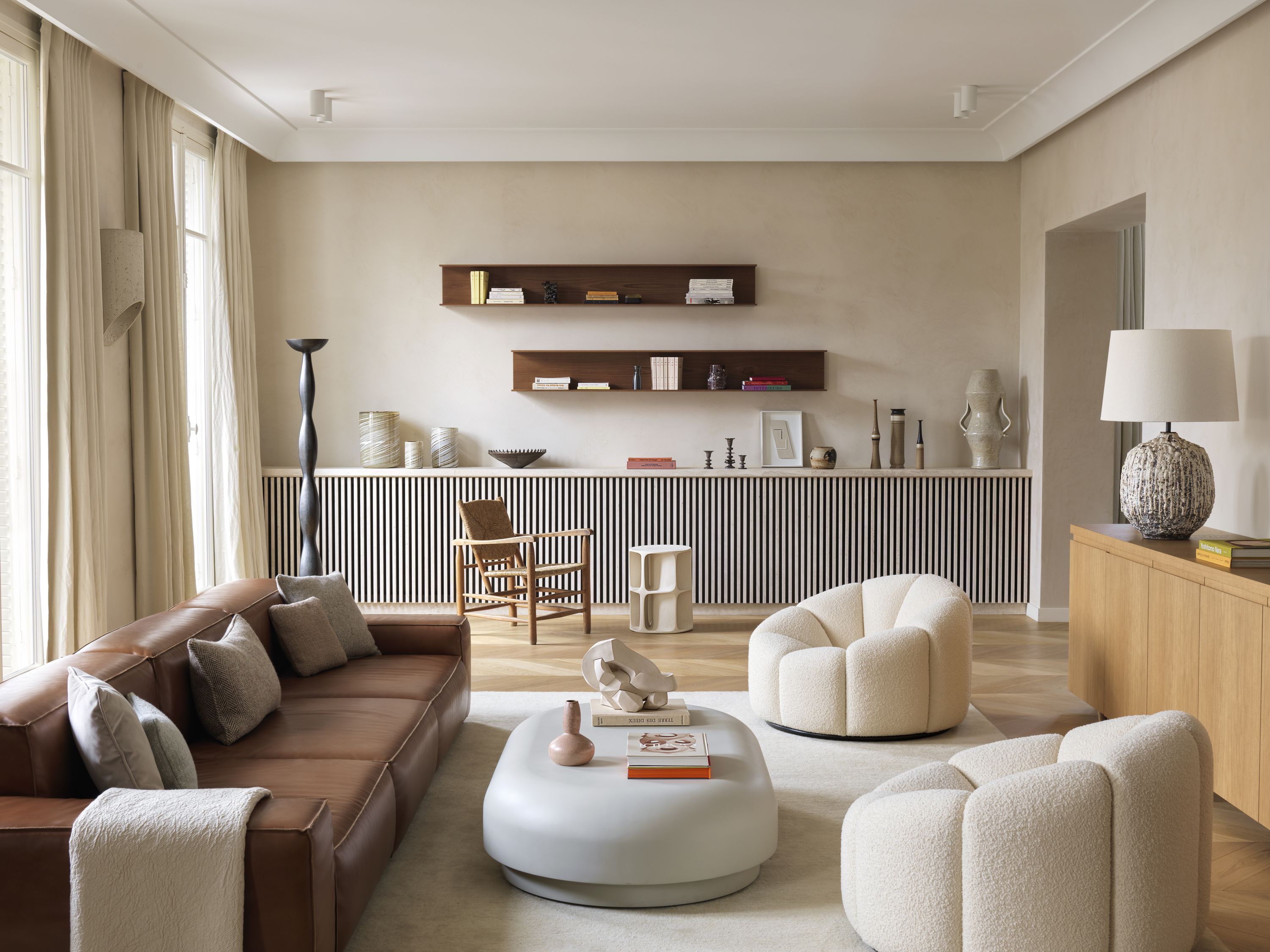 A living room with beige walls, cream chairs and a dark brown sofa