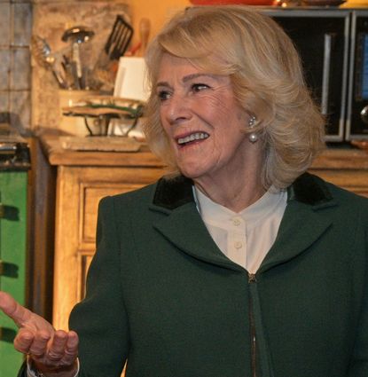 Queen Camilla wearing a green coat and smiling at a table with actress Victoria Smurfit