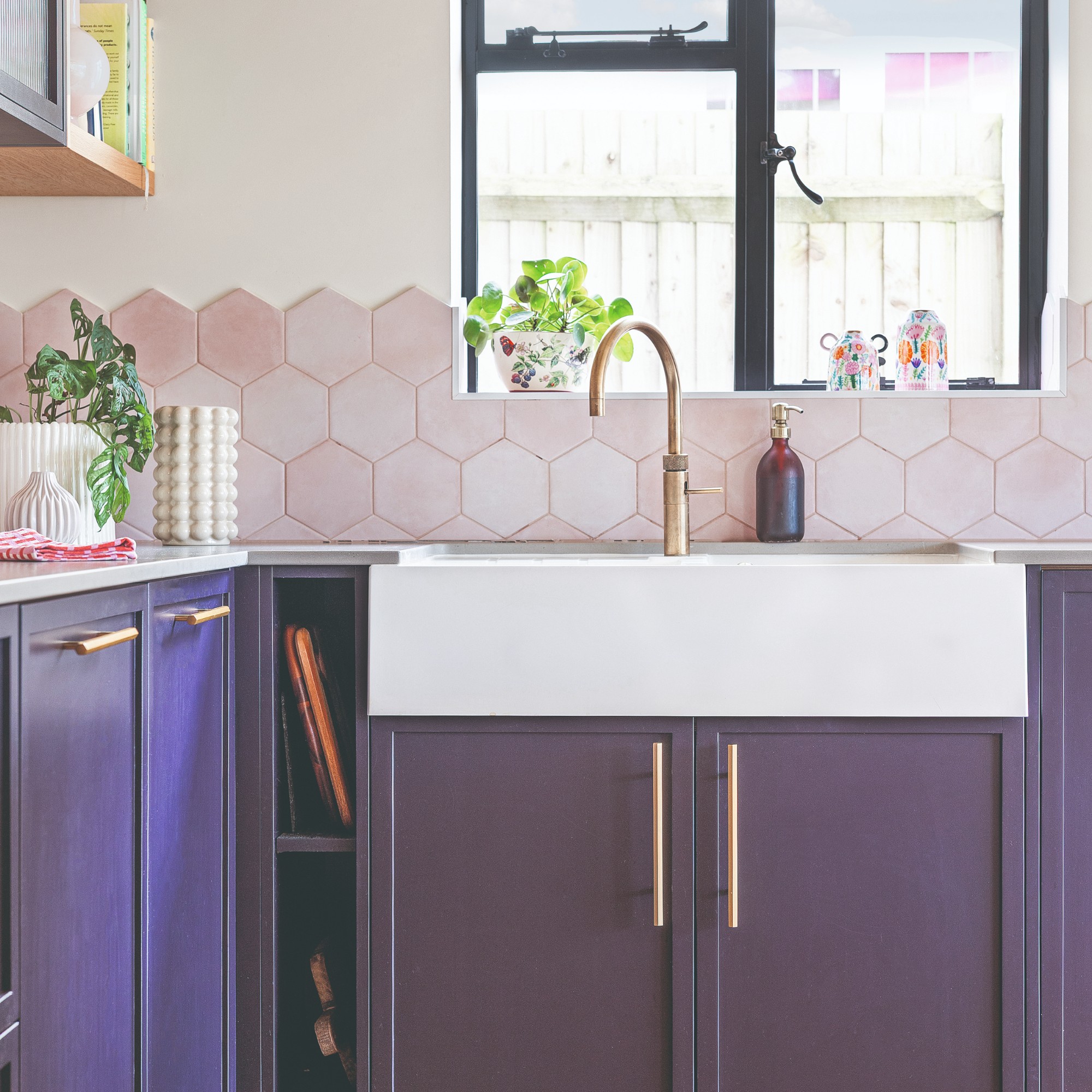A kitchen with purple cabinets and a pink tiled splashback