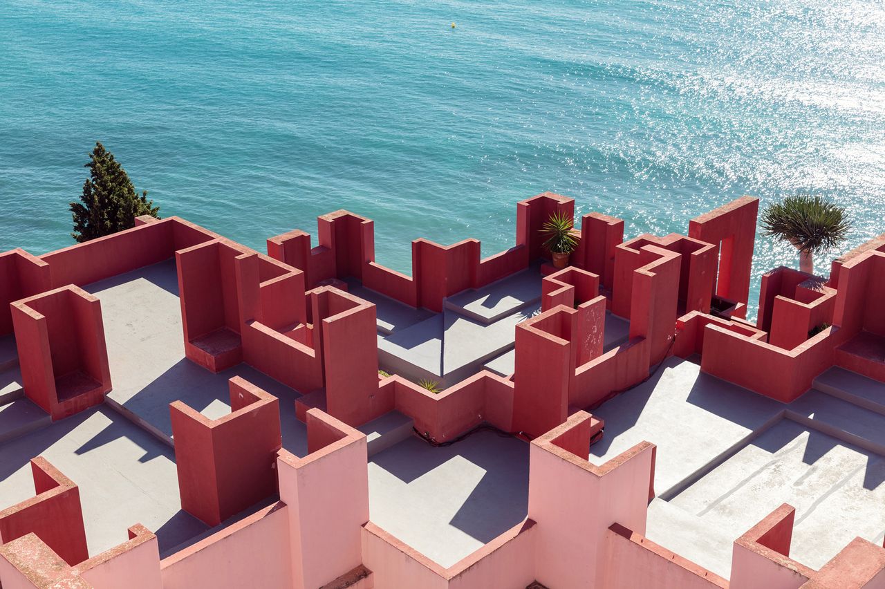 View from above of La Muralla Roja by Ricardo Bofill in Calp, Spain - the rooftop of the building featuring red and pink walls of varying heights beside the sea